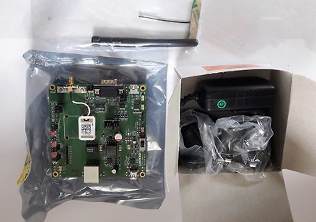 Leiterplatte in Plastikverpackung und Netzteil im Karton