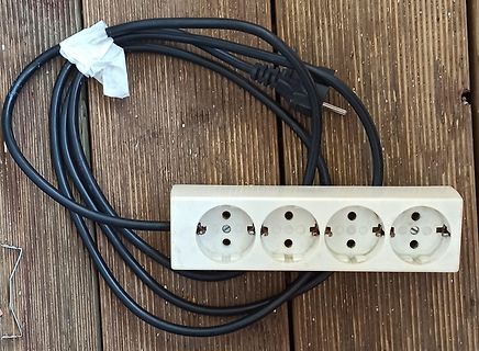 Mehrfachsteckdose mit schwarzem Kabel auf Holzuntergrund