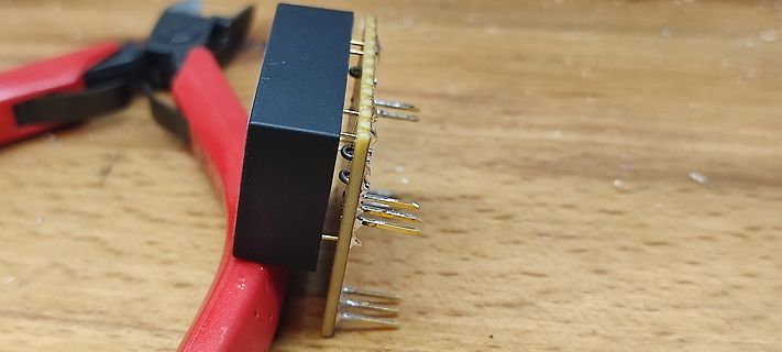 IC-Bauteil in einer Zange auf Holzuntergrund