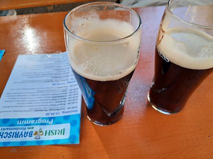 Zwei Gläser dunkles Bier auf einem Holztisch mit Programmflyer