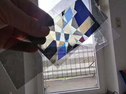 Hand hält ein buntes geometrisches Muster vor Fenster
