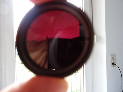 Hand hält ein rotes Filterglas vor einem Fenster