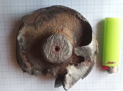 Beschädigtes Metallobjekt mit Feuerzeug zum Größenvergleich