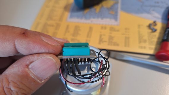 Hand hält Bauteil mit Kabeln auf Werkstattunterlage