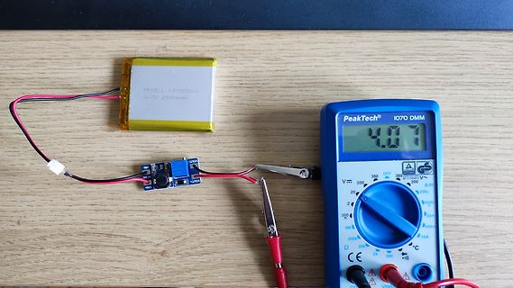 LiPo-Akku, Ladeplatine und Multimeter auf Holzuntergrund