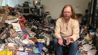 Mann sitzt in einem sehr unordentlichen Zimmer