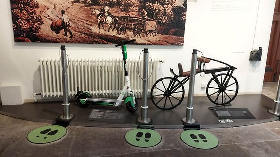 Museumsausstellung mit E-Scooter und historischem Wagen