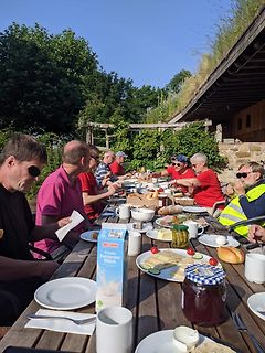 Menschen essen gemeinsam im Freien an einem Holztisch
