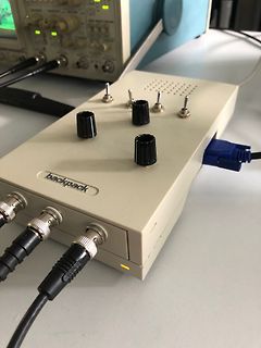 Elektronik-Messgerät mit Kabeln und Oszilloskop im Hintergrund