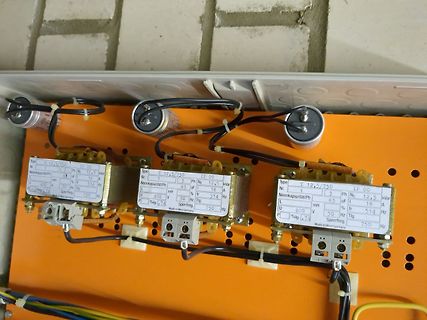 Drei Kondensatoren mit Typenschildern auf orangefarbenem Untergrund