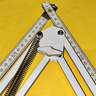 Maßband und weißes Metallteil auf gelbem Grund