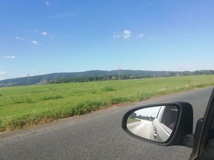 Landschaft mit Wiese, Hügeln und Rückspiegel eines Autos