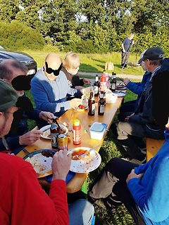 Menschen sitzen beim Essen an einem Holztisch im Freien