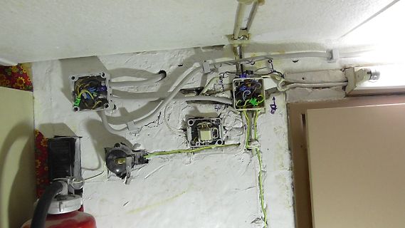 Freiliegende elektrische Leitungen und Schalterdosen an einer Wand