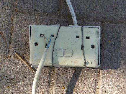 Defekte Steckdose auf Pflastersteinen