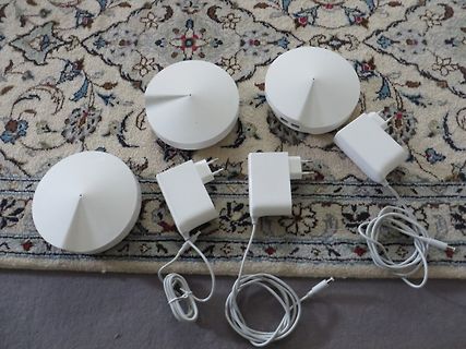Drei weiße Smart-Home-Geräte mit Netzteilen auf Teppich