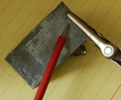 Metallplatte mit Bleistift und Zange auf Papier