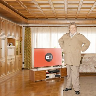 Mann steht in einem Wohnzimmer vor einem Fernseher