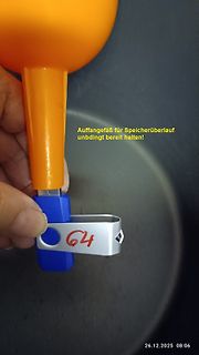 Hand hält orangefarbenes Bauteil mit Metallclip