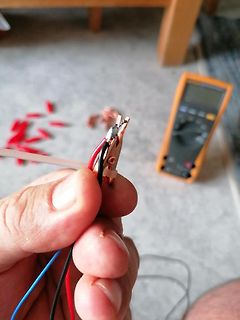 Hand hält Messkabel mit Krokodilklemme und Multimeter im Hintergrund