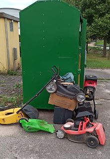 Mehrere Rasenmäher vor einem grünen Container