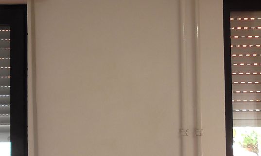 Weiße Wand mit zwei vertikalen Rohren und Fensterjalousien