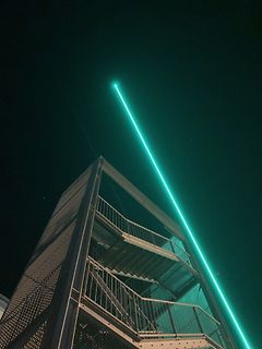 Grüner Laserstrahl über Metalltreppe bei Nacht