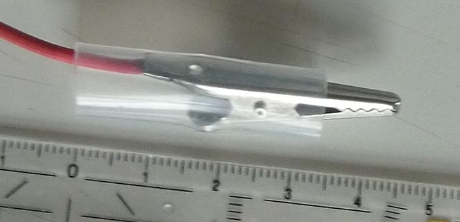 Krokodilklemme an rotem Kabel mit Lineal