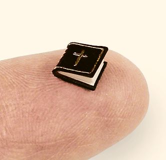 Miniatur-Buch mit Kreuz auf einem Finger