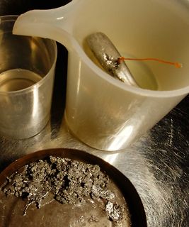 Metallklumpen und Metallstück in Becherglas