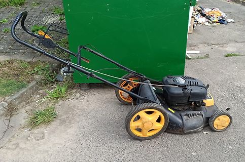 Rasenmäher auf Asphalt vor grünem Container