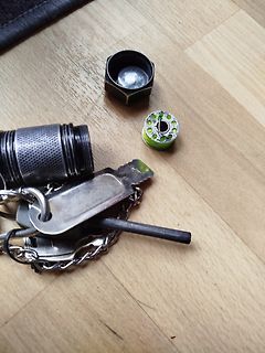 Schlüssel, Taschenlampe und Zylinderbauteil auf Holzuntergrund