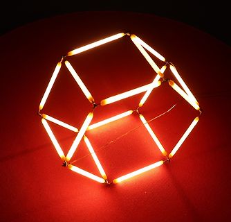 Leuchtender Würfel aus LED-Stäben auf rotem Grund