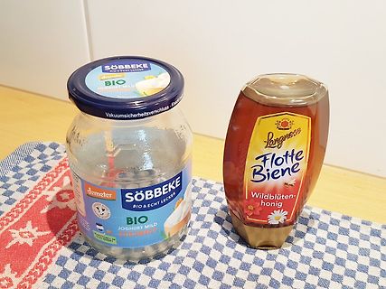 Joghurtglas und Honigflasche auf Tischdecke