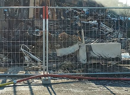 Trümmer eines abgebrannten Gebäudes hinter Bauzaun