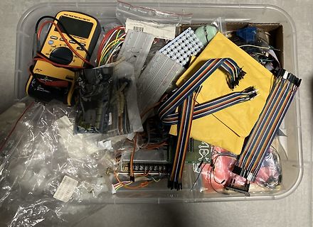 Kiste mit Elektronikbauteilen, Multimeter und Flachbandkabeln