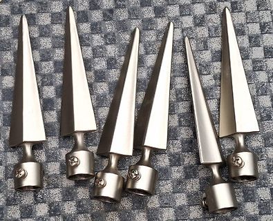 Sechs metallische, spitze Bauteile auf grauem Untergrund