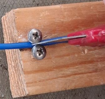 Blaues Kabel wird mit einer Zange auf Holzbrett bearbeitet