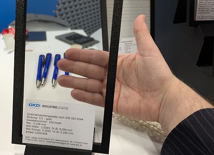 Hand hält ein Textschild vor einem Gewebe