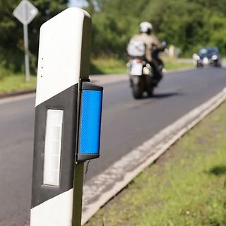 Leitpfosten an einer Straße mit Motorrad im Hintergrund