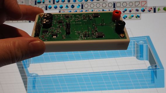 Hand hält bestückte Leiterplatte vor CAD-Modell