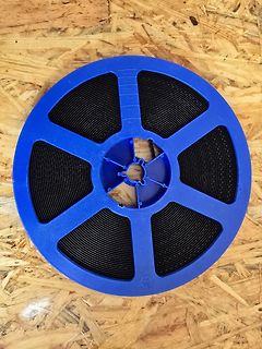 Blaue Spule mit schwarzem Draht auf Holzuntergrund