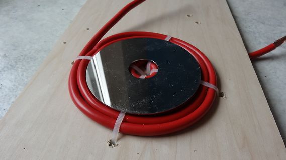 Rote Kabelrolle mit Metallscheibe auf Holzbrett