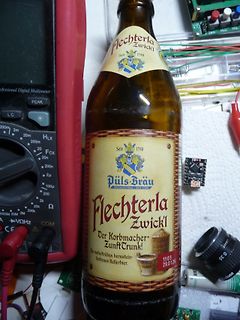 Multimeter, Bierflasche und Elektronikbauteile auf Werkstattunterlage