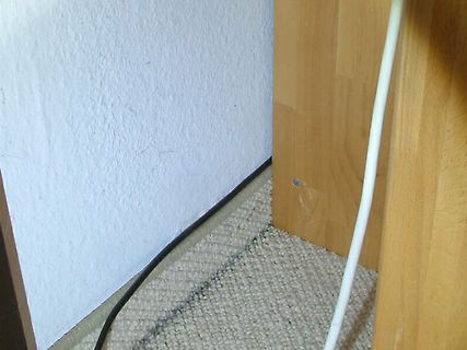 Ecke eines Raumes mit Wand, Teppich und Kabeln