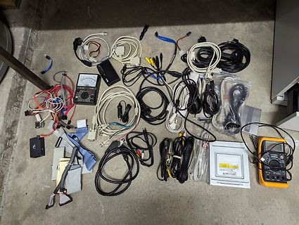 Verschiedene Kabel, Netzteile und Messgeräte auf Boden