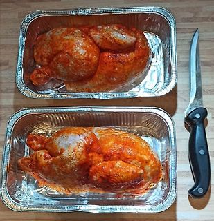 Zwei marinierte Hähnchen in Aluschalen mit Messer
