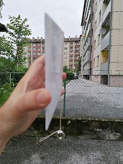 Hand hält ein weißes Blatt Papier vor einem Gebäude
