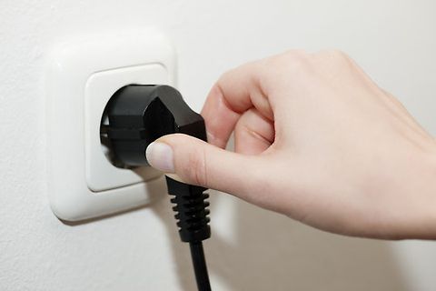 Hand steckt schwarzen Netzstecker in Steckdose